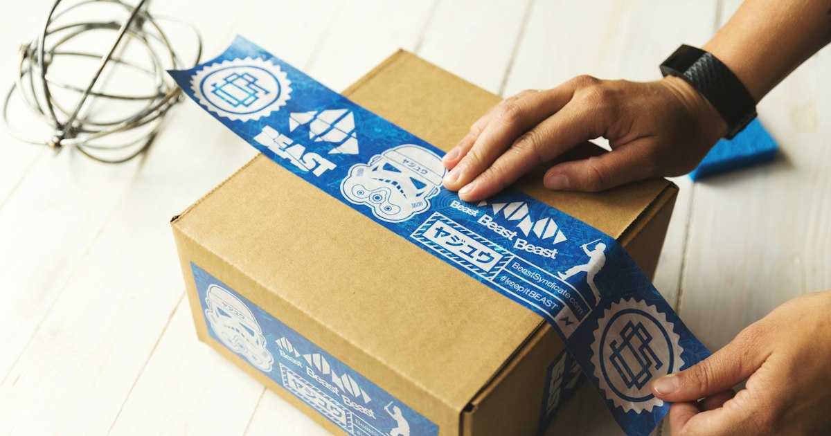 Manos cerrando una caja de cartón con cinta adhesiva