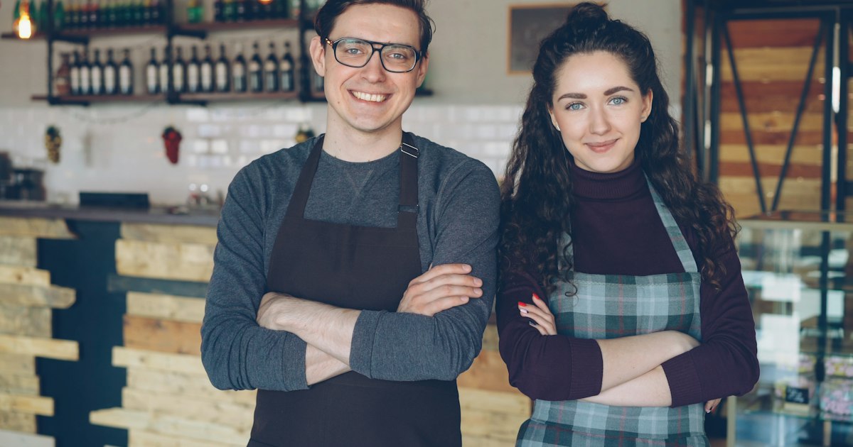 Dos dueños de una cafetería sonriendo delante del mostrador