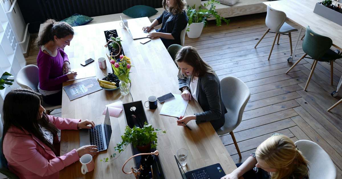 Personas trabajando con portátiles en una mesa larga de coworking