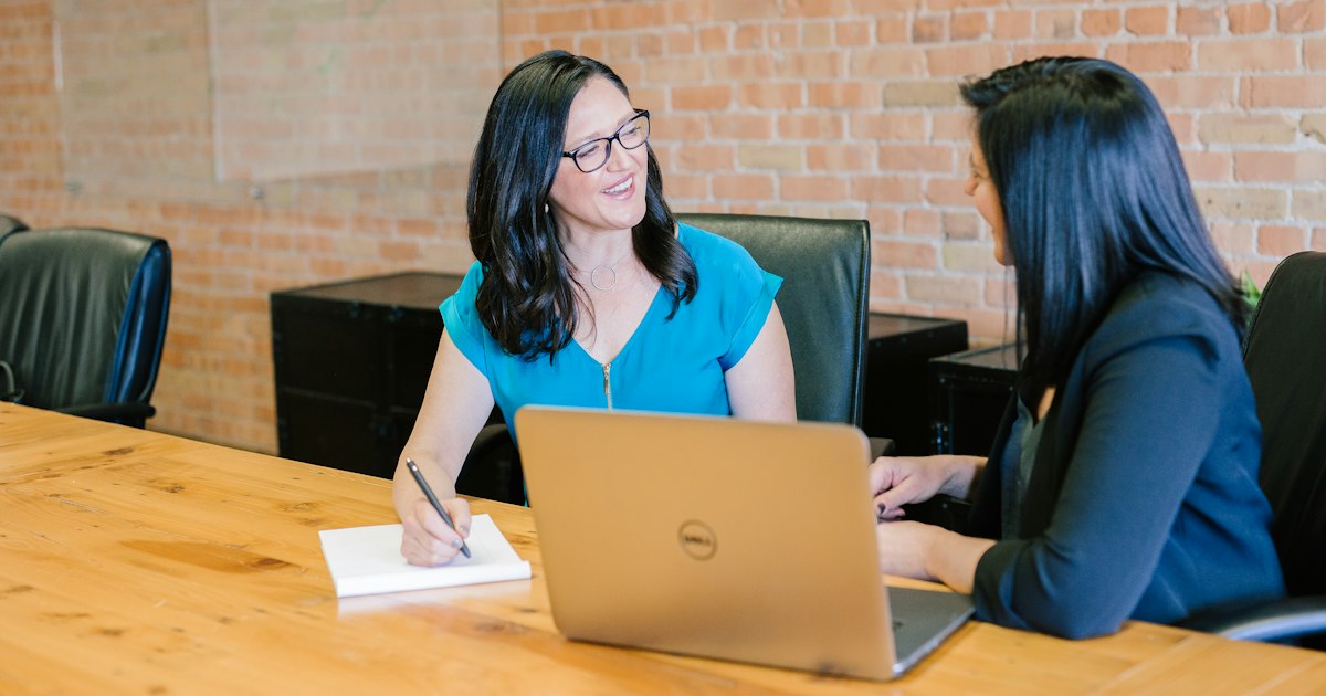 Dos mujeres conversando en una reunión de trabajo con un portátil