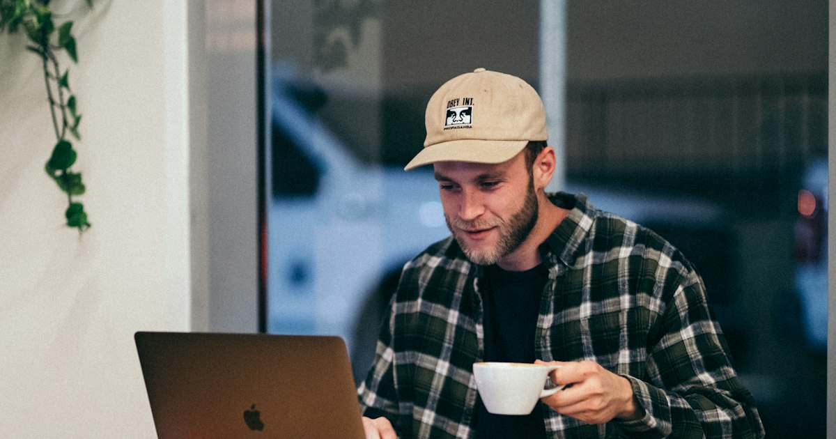 Hombre usando un portátil con un café en la mano