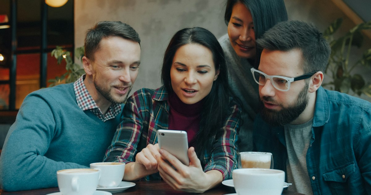 Cuatro amigos mirando juntos un móvil en una cafetería