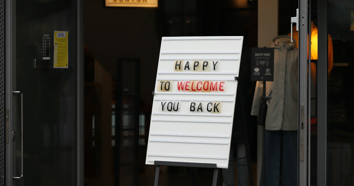 Cartel en la puerta de una tienda con el texto «Happy to welcome you back»