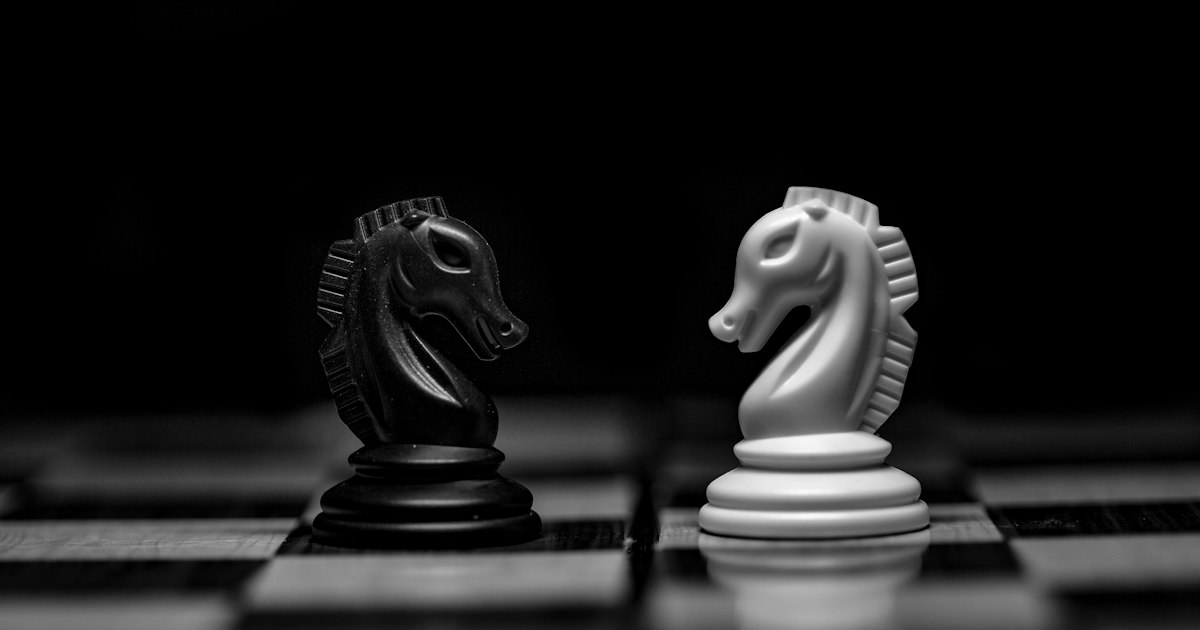 Dos caballos de ajedrez, uno negro y uno blanco, frente a frente