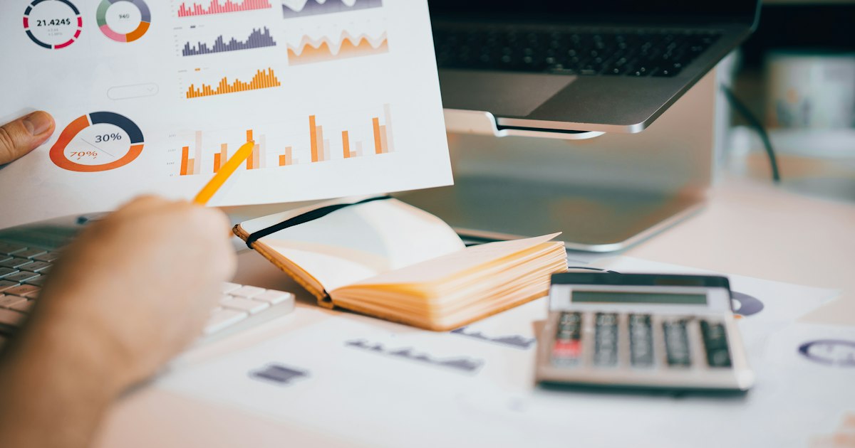 Persona revisando gráficos impresos junto a un portátil y una calculadora